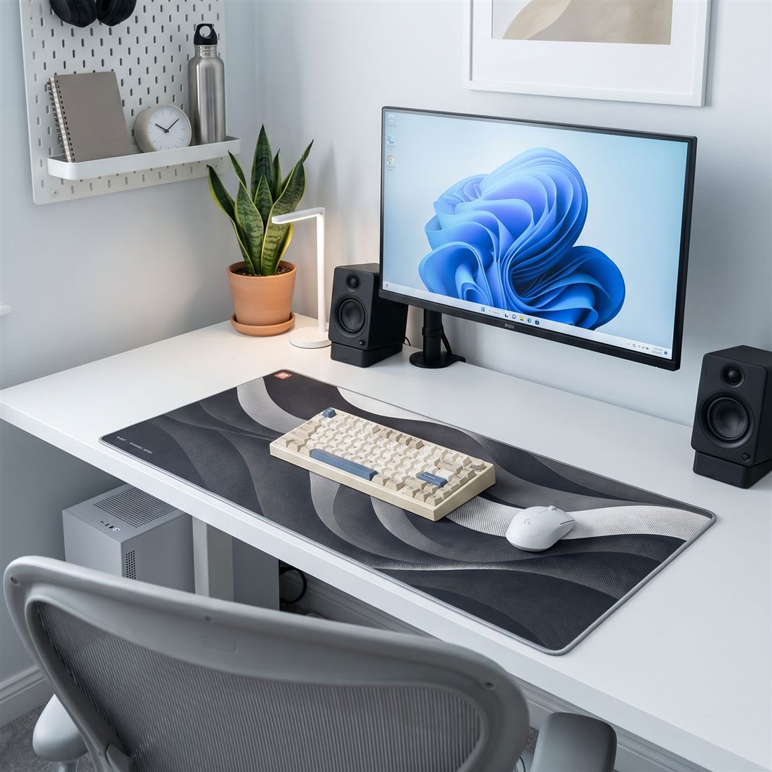 A finished desk setup with a BACKSTOCK desk mat, speakers, lamp and greenery